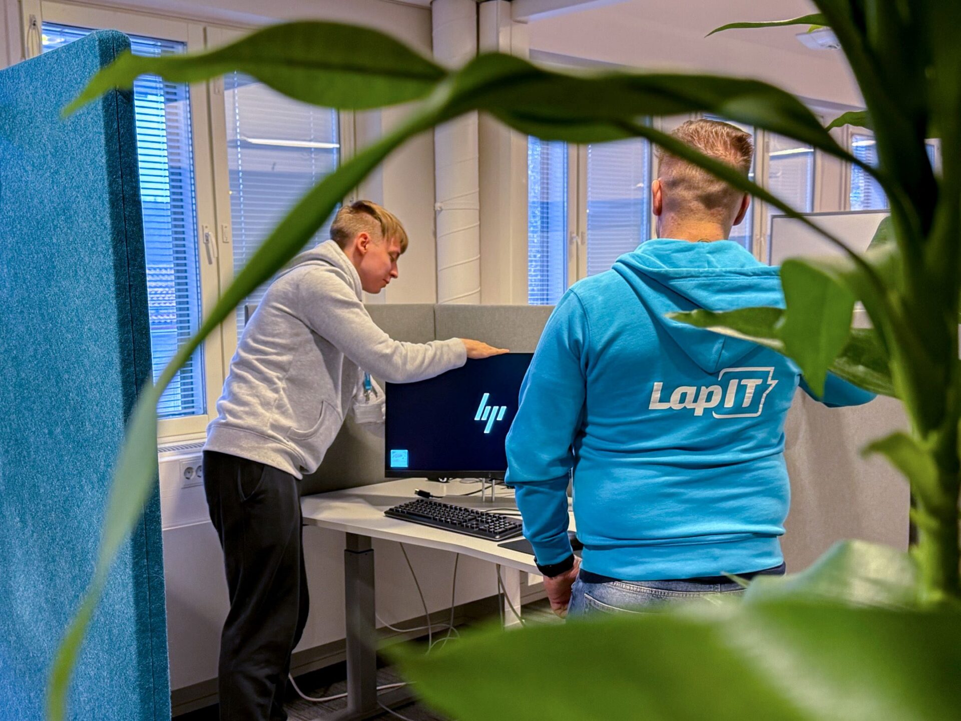 Kaksi työntekijää asentamassa tietokonetta toimistotilassa.